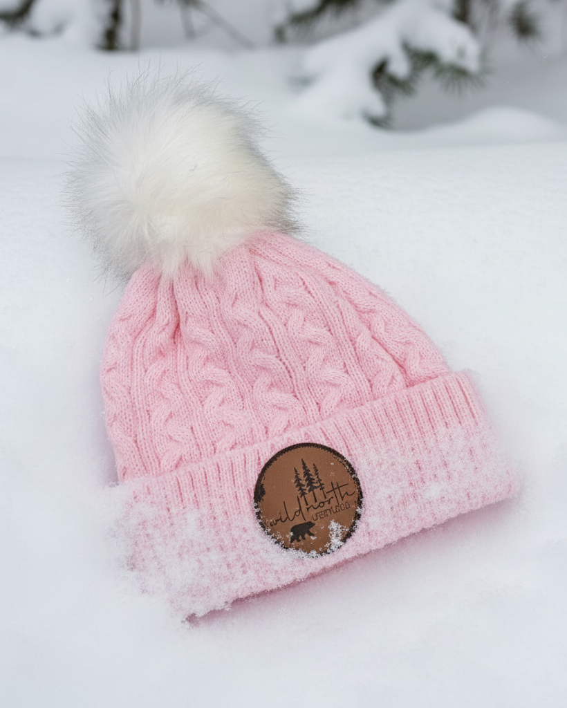 Pink knit beanie with a fur pom-pom on a snowy background