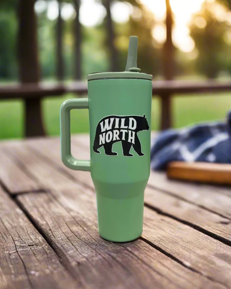 Green tumbler with 'Wild North' bear graphic on a wooden surface
