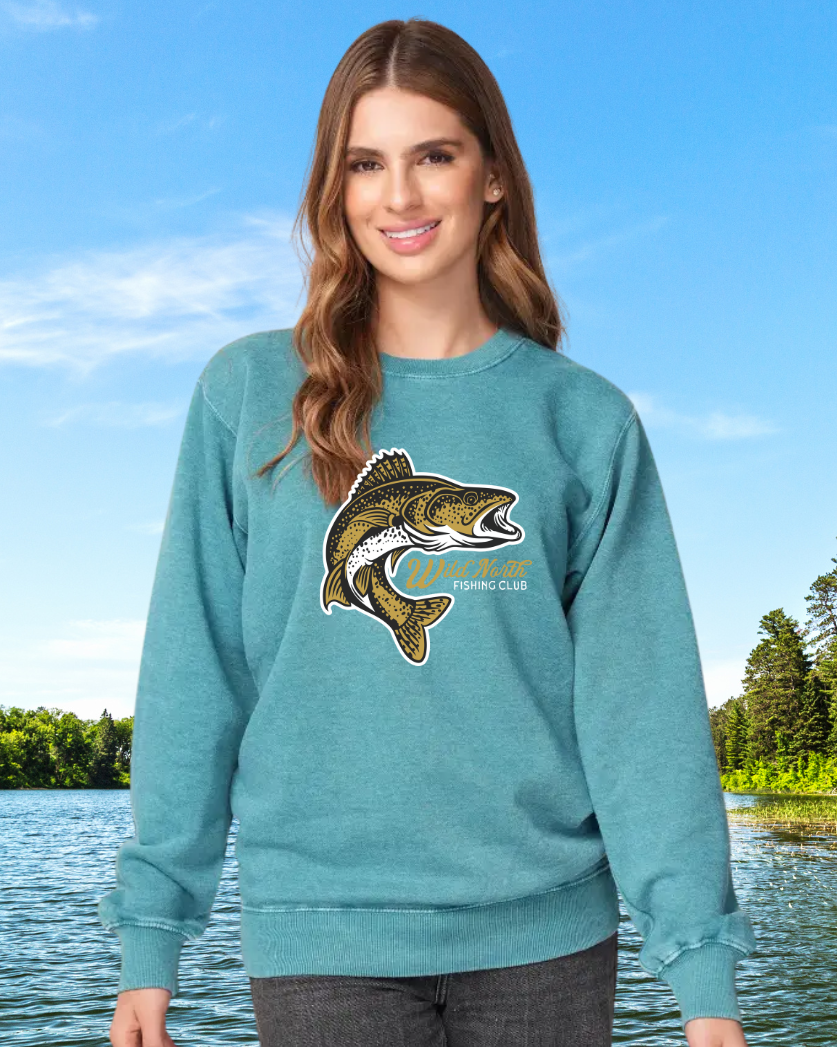 Woman wearing a teal sweatshirt with a fish graphic in front of a lake and trees