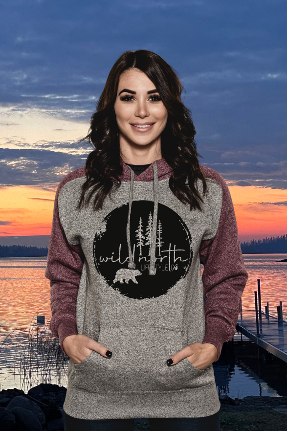 Woman wearing a hoodie with a nature graphic at sunset by a lake