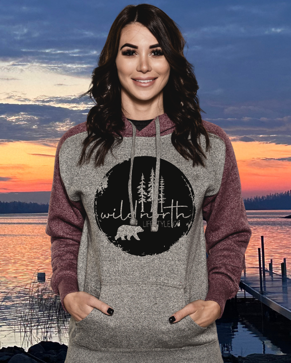 Woman wearing a hoodie with a nature graphic at sunset by a lake