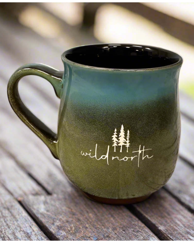 A ceramic mug with a variegated glaze in green and black colors, featuring the text 'wildnorth' on the side, placed on a wooden surface.