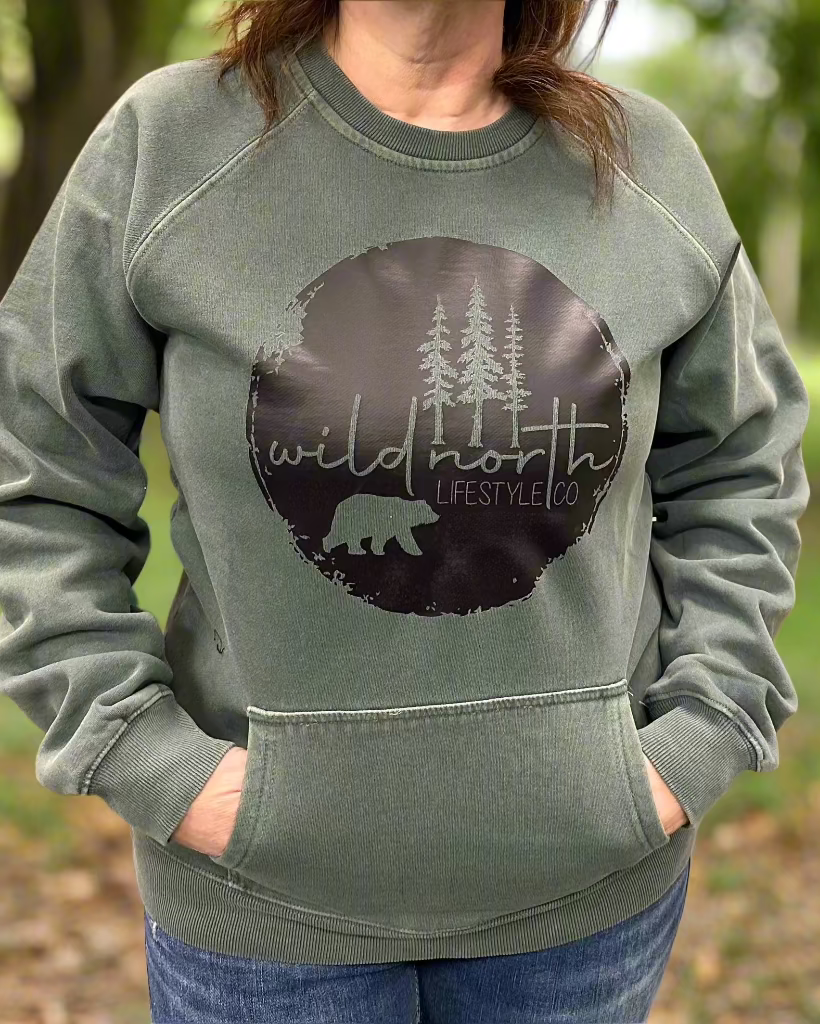 A person standing outdoors wearing a gray crew neck sweatshirt with the text 'Wild North' and a stylized bear logo on the front.