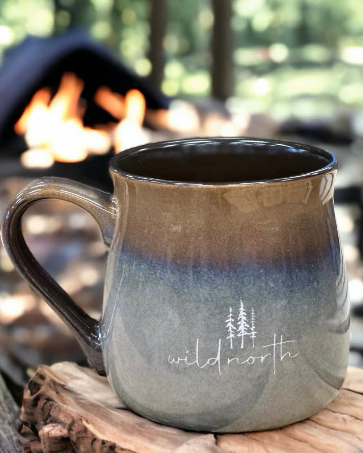 A ceramic mug with a variegated glaze in green and black colors, featuring the text 'wildnorth' on the side, placed on a wooden surface.